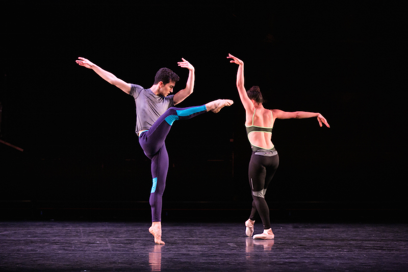 Anthony Huxley balances in an attitude in the front while Rachel Hutsell tendus with her back facing the audience